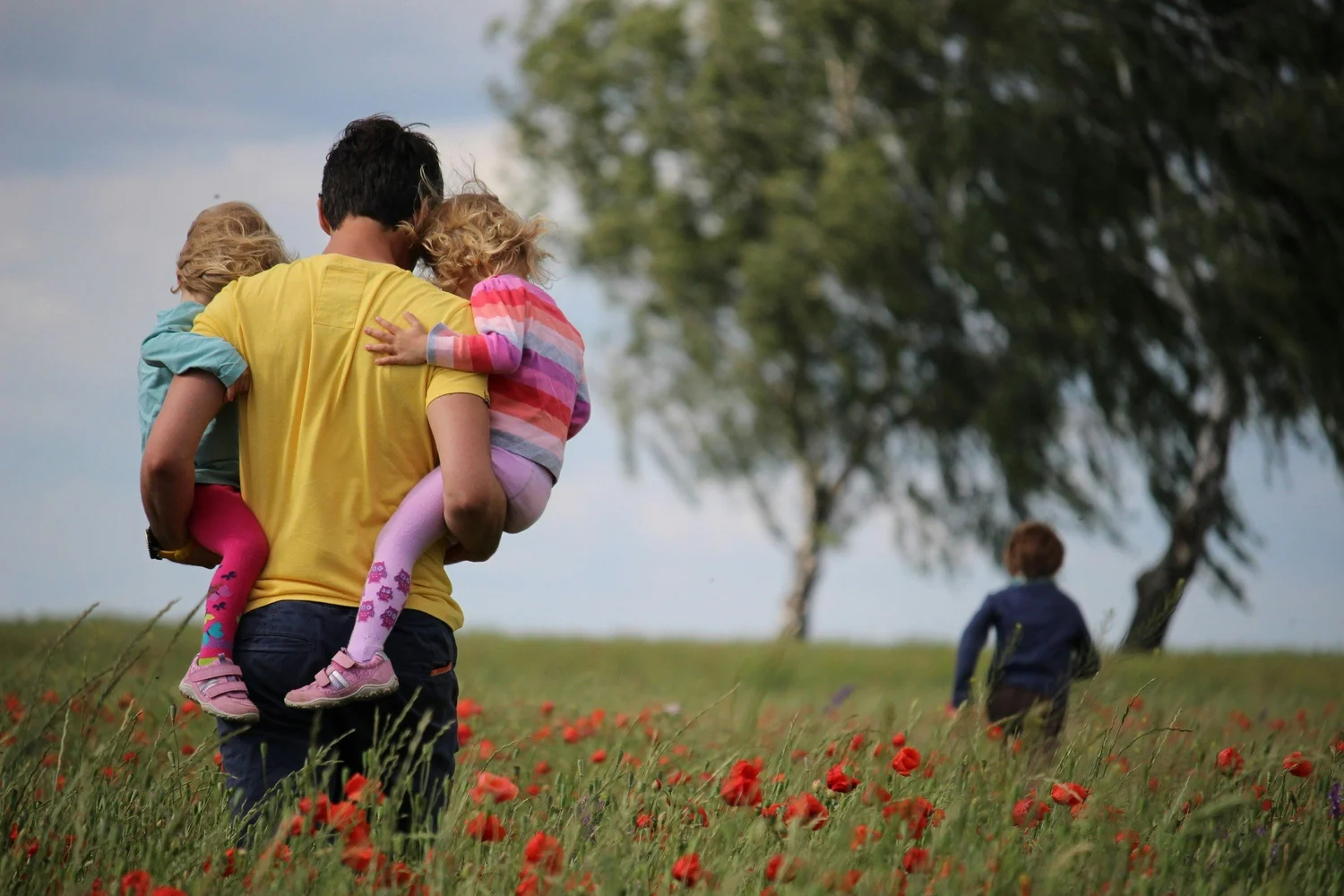 A father carrying two children through a field of red flowers.